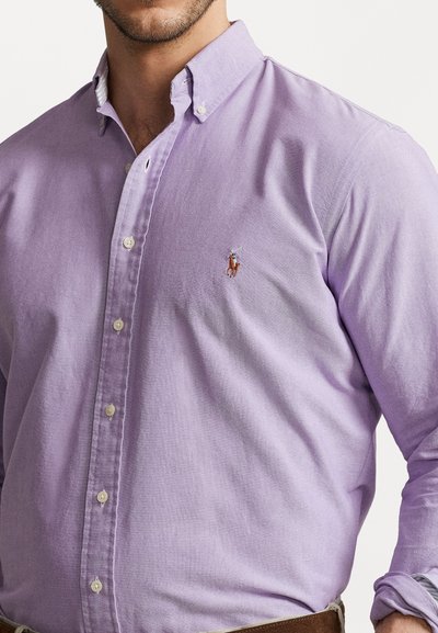 Ανοικτό μωβ πουκάμισο με κουμπιά, κατασκευασμένο από ύφασμα με υφή. Περιλαμβάνει ένα μικρό κεντημένο λογότυπο στο στήθος και κλασικό σχέδιο γιακά.