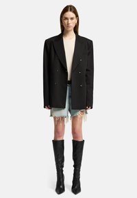 Blazer nero oversize a doppio petto, top beige attillato, shorts in denim strappati e stivali alti neri a punta. Accessori semplici inclusi.