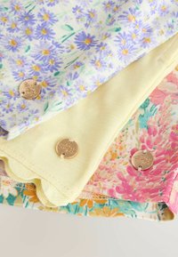 Három összehajtott virágmintás anyagrészlet lila, sárga és rózsaszín árnyalatokban, mindegyiken egy-egy kisméretű, kerek arany virágdísz.