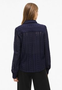 Mørkeblå åbenstrikket bluse med lange ærmer, detaljeret tekstur og krave, med knapmanchetter og en rund kant.