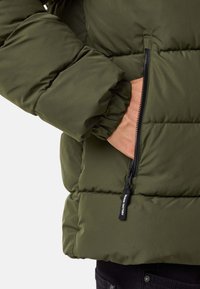 Oliwkowa kurtka puchowa z pikowanym wzorem, z zapinaną na zamek kieszenią i elastycznymi mankietami. Gładka, matowa tekstura tkaniny.