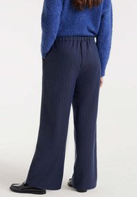Pantalones de pierna ancha a rayas en azul marino con un ajuste relajado y cinturilla elástica, combinados con un suéter texturado azul. Incluye bolsillos laterales.