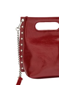 Czerwona torebka z sztucznej skóry o błyszczącym wykończeniu, z wycięciem na górnym uchwycie i srebrnymi ćwiekami po jednej stronie. Zawiera również szczegół z łańcuszkiem.