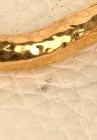 Gros plan d'une bague dorée brillante reposant sur un tissu matelassé écru texturé avec de petites taches sombres.