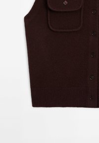 Gilet sans manches tricoté marron foncé avec fermeture à boutons et poche à rabat sur la poitrine, ourlet côtelé, présenté sur fond blanc.