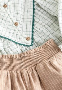 Grön- och vitrutigt linne med scallopdetaljer och träknappar, kombinerat med en beige randig kjol med smockat midja. Mjuka, texturerade tyger.