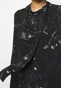 Černý top z látky s nebeskými vzory hvězd a souhvězdí, s designem s smyčkovým krkem a měkkými zavěšenými rukávy.