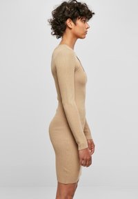 Robe tricotée côtelée beige avec des manches longues, décolleté en V et silhouette ajustée, dotée d'un ourlet au genou et d'un tissu texturé.