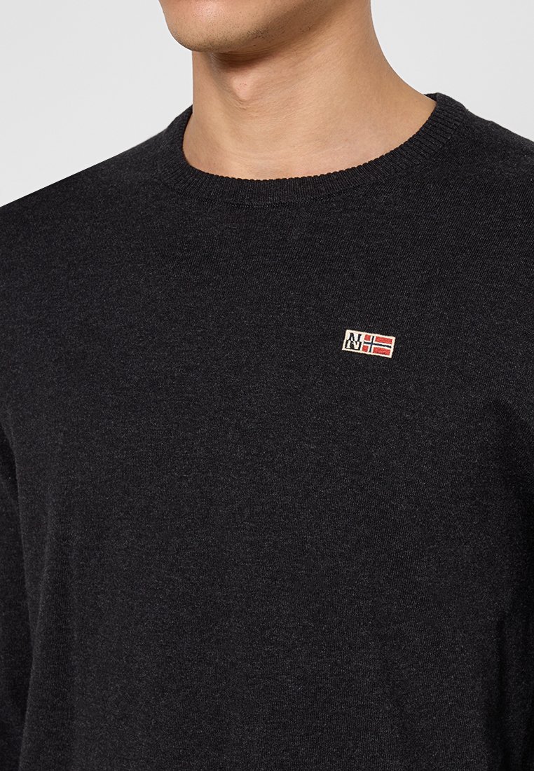 Pull en tricot noir à col rond, avec un petit patch logo brodé en rouge, blanc et bleu sur la poitrine gauche. Texture douce.