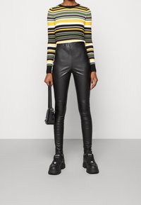 Person som bär en randig långärmad tröja, högmidjade svarta läderbyxor, svarta klumpiga sneakers och håller en liten svart handväska.