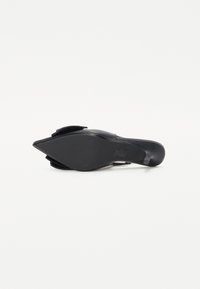 Svart høyhælte sko med spiss tå, glatt skinnoberdel og en teksturert, friksjonsbehandlet såle for bedre grep. Har en slip-on-design med en dekorativ detalj.