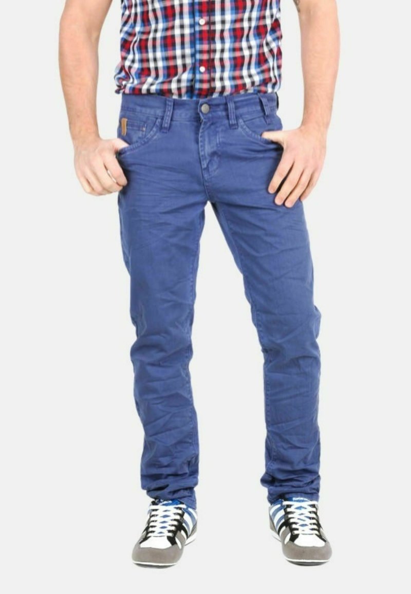 Pantalones de algodón azul con un ajuste slim, que cuentan con bolsillos frontales y cierre de botón. Se llevan con zapatillas negras y blancas y una camisa de cuadro.