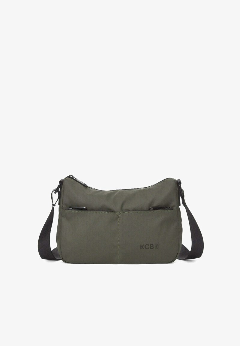 Bolso bandolera verde oliva hecho de tela duradera. Cuenta con cierre de cremallera, dos bolsillos frontales y una correa negra ajustable. Logo de KCB visible.