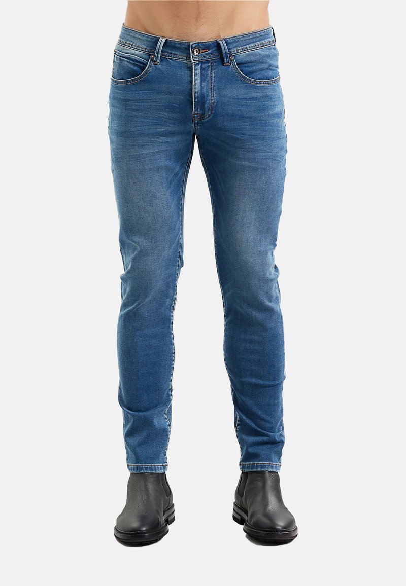 Jeans di denim blu con taglio aderente, cinque tasche e leggero scolorimento. Abbinati a stivaletti neri alla caviglia. Tessuto liscio, design classico.