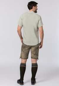 Hellgrünes kurzärmliges Hemd, beiger Shorts mit ausgewaschenem Muster und dunklen knielangen Socken mit gestricktem Muster, schwarze Schuhe.