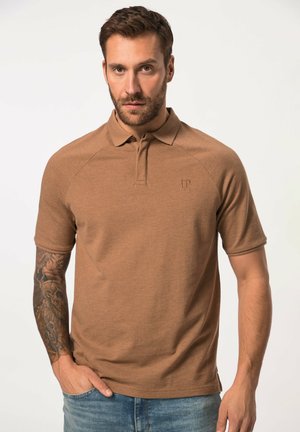 Braunes Poloshirt aus weichem Stoff, mit Kragen, kurzen Ärmeln und einem dezenten Logo auf der Brust; kombiniert mit hellblauen Jeans.