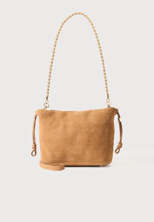 Bolso bandolera de ante color tostado con correa de cadena en tono dorado y cordones laterales ajustables anudados, sobre un fondo liso y claro.
