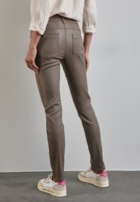 Bruna slim-fit byxor med en slät textur, med bakfickor och kontrasterande sömmar på sidorna, tillsammans med vita sneakers med rosa detaljer.