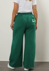Grüne, weit geschnittene Sweatpants mit Zugbandbund, ausgestattet mit einer Gesäßtasche, auf der "LA" in Weiß gedruckt ist. Hergestellt aus einem weichen, strukturierten Stoff.