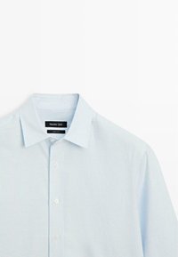 Camicia a righe celesti con collo a camicia, chiusura frontale con bottoni e deboli linee verticali. Realizzata in un tessuto liscio. Etichetta del marchio visibile.