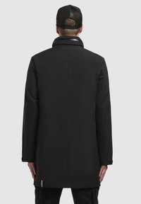 Abrigo largo negro con una textura suave, que presenta un cuello alto y un diseño elegante. La parte trasera muestra una silueta limpia con un mínimo de detalles.