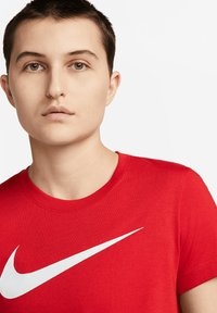 Červené bavlněné tričko s kulatým výstřihem a krátkými rukávy, se silným bílým logem Nike swoosh přes hruď.