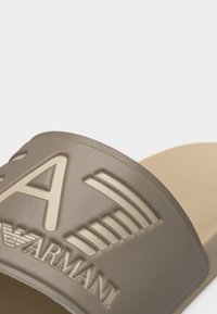 Μπεζ σανδάλι slide με ανάγλυφο λογότυπο ARMANI και στυλιζαρισμένο έμβλημα αετού στη φαρδιά λωρίδα πάνω από το πάνω μέρος.