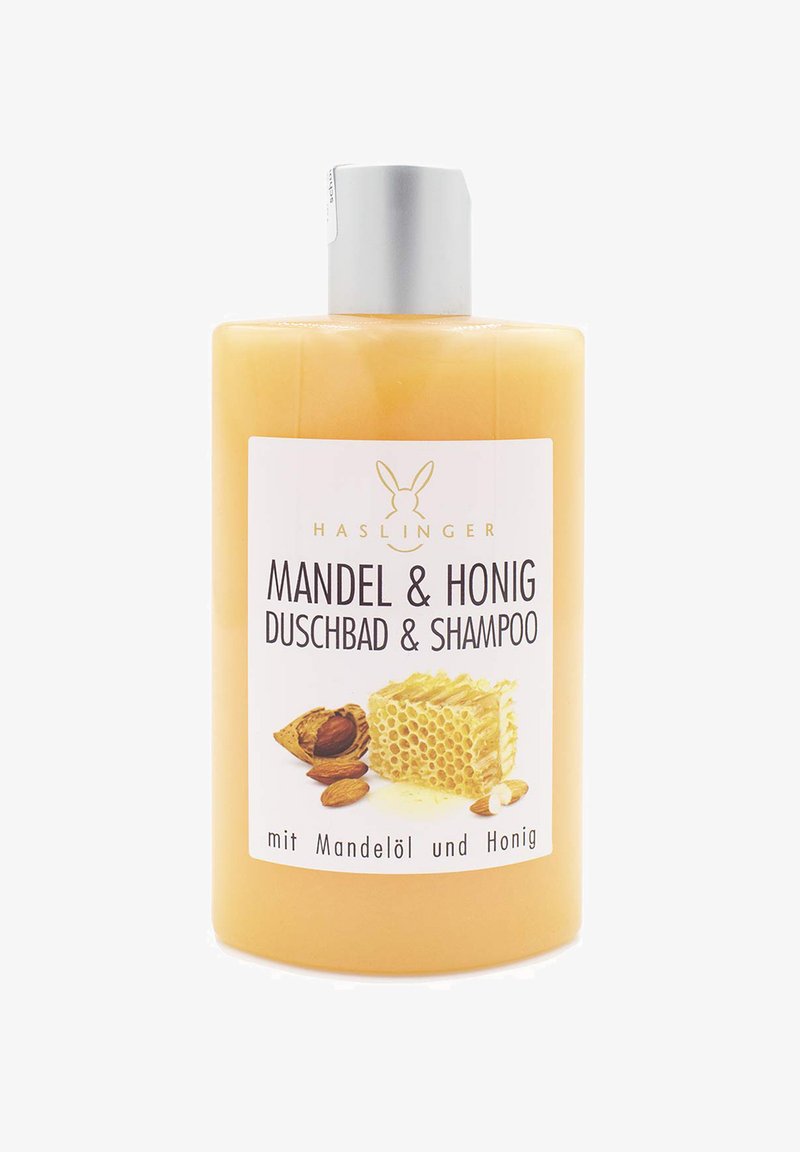 Flasche mit Mandel- und Honig-Duschgel und Shampoo; durchsichtige gelbe Flüssigkeit, silberner Deckel, weißes Etikett mit schwarzem Text und Produktbild.