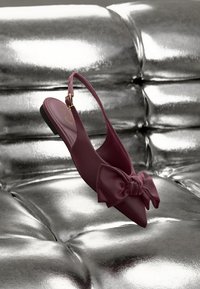 Burgundi slingback lapos cipő hegyes orral és nagy masni részlettel. Simább anyagból készült, kis arany csatt díszítéssel.