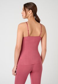 Débardeur rose avec des bretelles réglables, fabriqué en tissu doux. Design ajusté avec une texture lisse, arrivant jusqu'aux hanches.