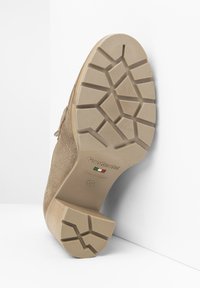 Zapato de ante beige con suela de goma texturizada. La suela presenta un patrón de relieve multidireccional. Logo y talla estampados visibles.