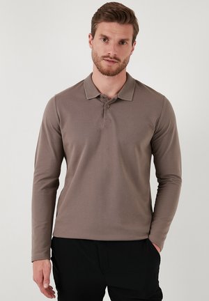 Camisa polo de manga larga en tono topo con cuello, dos botones y un tejido texturizado, combinada con pantalones negros. Diseño simple, forma ajustada.