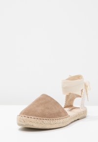 Espadrilles in suede marrone con punta affusolata, lati in tessuto intrecciato e cinturino alla caviglia regolabile beige. Suola in giuta naturale.