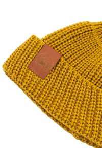 Wełniana czapka w kolorze musztardowym z teksturowanym wzorem. Posiada brązową skórzaną łatę z wytłoczonym wzorem gór.