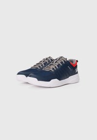 Baskets de sport marine avec une tige texturée, lacets gris clair, accents rouges au niveau du talon et une semelle en caoutchouc blanche présentant un motif en nid d'abeille.