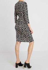 Robe à imprimé léopard beige et noir, longueur au genou, manches trois-quarts et taille cintrée, associée à des mules à talons blocs noires.