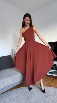 Rozsdaszínű, egyrészes vállat szabadon hagyó ruha, testhezálló felsőrésszel és bő szoknyával. Sima anyagból készült, térdig érő hosszúságú, fekete magassarkú cipővel viselve.