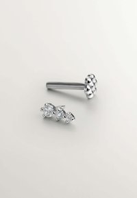 Pendientes de plata con tachuelas que presentan tres gemas transparentes de tamaños variables, diseñados con un acento floral suave y redondeado en uno de los pendientes.