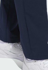 Marinblå träningsbyxor med en slät yta, med rak passform; kombinerat med vita sneakers som har perforerade detaljer.