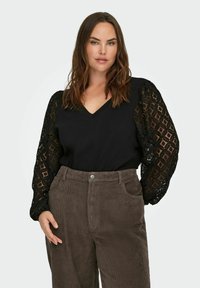 Czarny top z koronkowymi, bufkami w geometryczny wzór, zestawiony z brązowymi spodniami z sztruksu z przednimi kieszeniami i zapięciem na guziki.