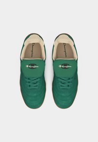 Ζευγάρι πράσινα αθλητικά παπούτσια Champion με μπεζ εσωτερική επένδυση, κορδόνια και λογότυπο στη γλώσσα, παρουσιάζονται από την κορυφή σε λευκό φόντο.