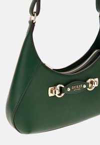 Bolso de mano texturizado verde con herrajes en tono dorado, que presenta un cierre con cremallera y un acento de logo en la parte frontal. Correa de hombro ajustable incluida.