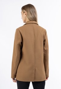 Cappotto marrone su misura con colletto a punta, maniche lunghe e vestibilità dritta. Presenta una cucitura posteriore pulita e una texture morbida.