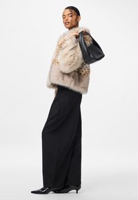Beżowa kurtka z sztucznego futra w cętkowany wzór, zestawiona z czarnymi szerokimi spodniami i teksturowaną czarną torbą. Stylizację dopełniają buty na obcasie.