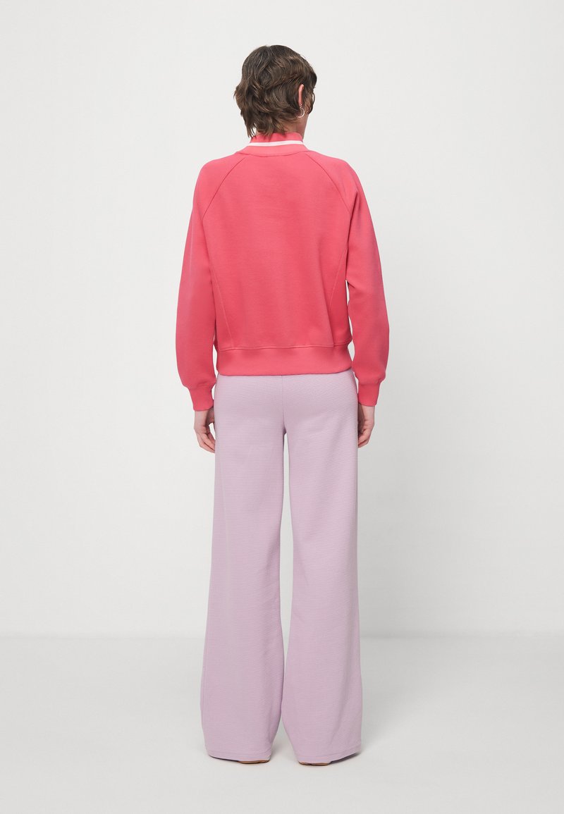 Felpa corallo con polsini e orlo a coste, abbinata a pantaloni larghi color lilla con un motivo testurizzato, vista da dietro.