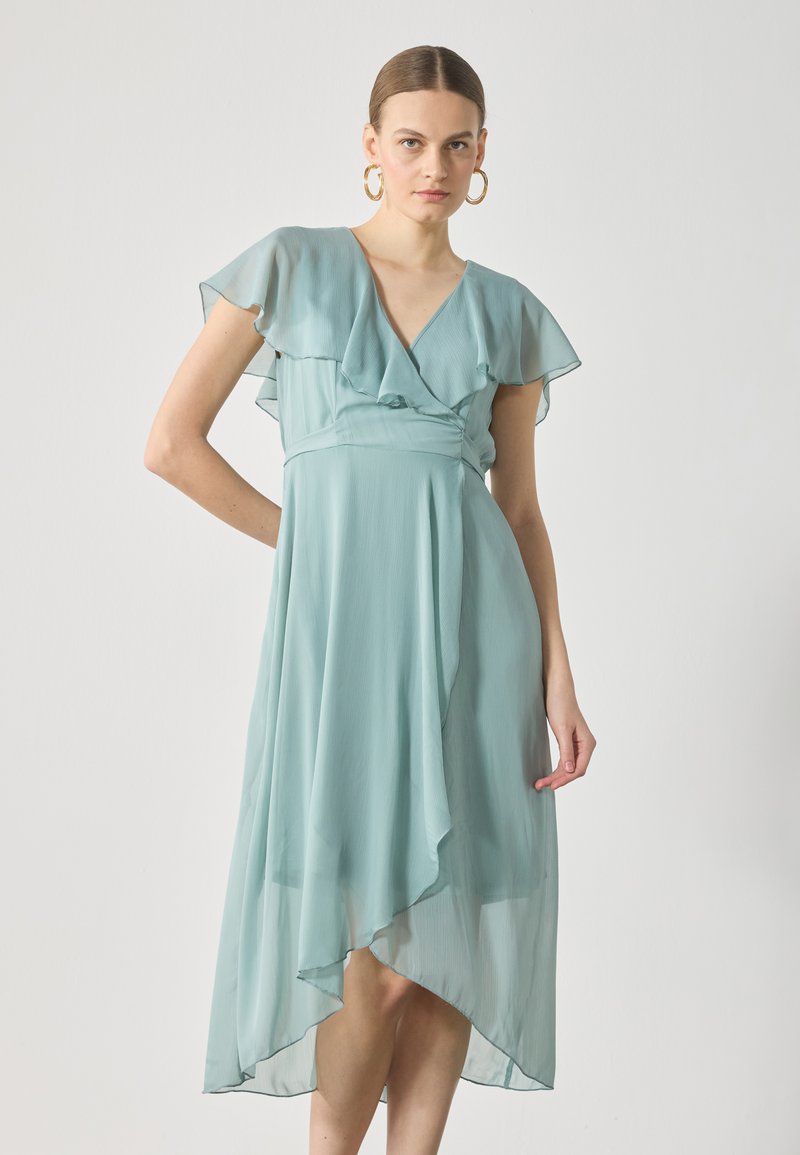 En ljus teal, midilång klänning gjord av genomskinligt tyg med volangärmar och en omslagdesign, med en asymmetrisk fåll.