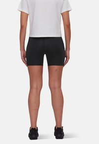 Pantaloni sportivi neri a vestibilità aderente, con una texture liscia e cuciture a contrasto, abbinati a una maglietta bianca corta e sneakers nere.