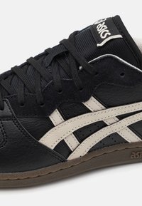 Baskets en cuir noir avec des rayures crème, tige texturée et lacets noirs. Comprend un col rembourré et le logo Asics sur la languette.