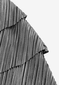 Tissu plissé noir avec un motif texturé. Présente une volute superposée le long du bord supérieur, créant un design ondulé.