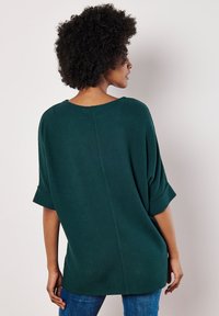 Lässiger, dunkelgrüner Pullover mit strukturiertem Strick, weiten Ärmeln und Rundhalsausschnitt, kombiniert mit blauen Jeans.